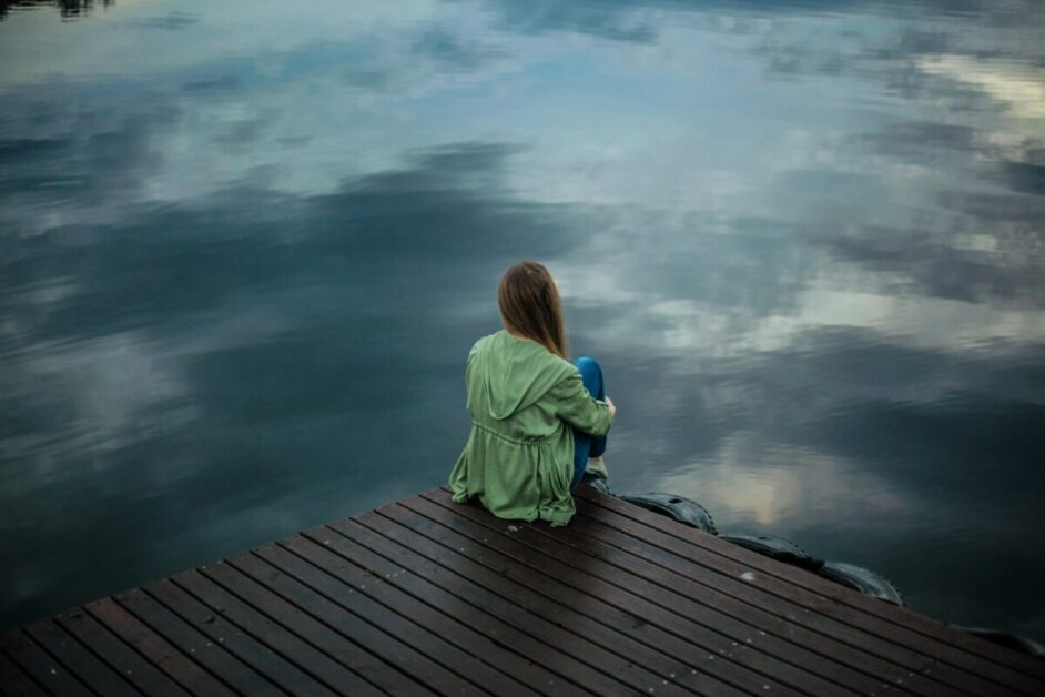 Individual sitting on a dock, reflecting by the water to build resilience and manage stress