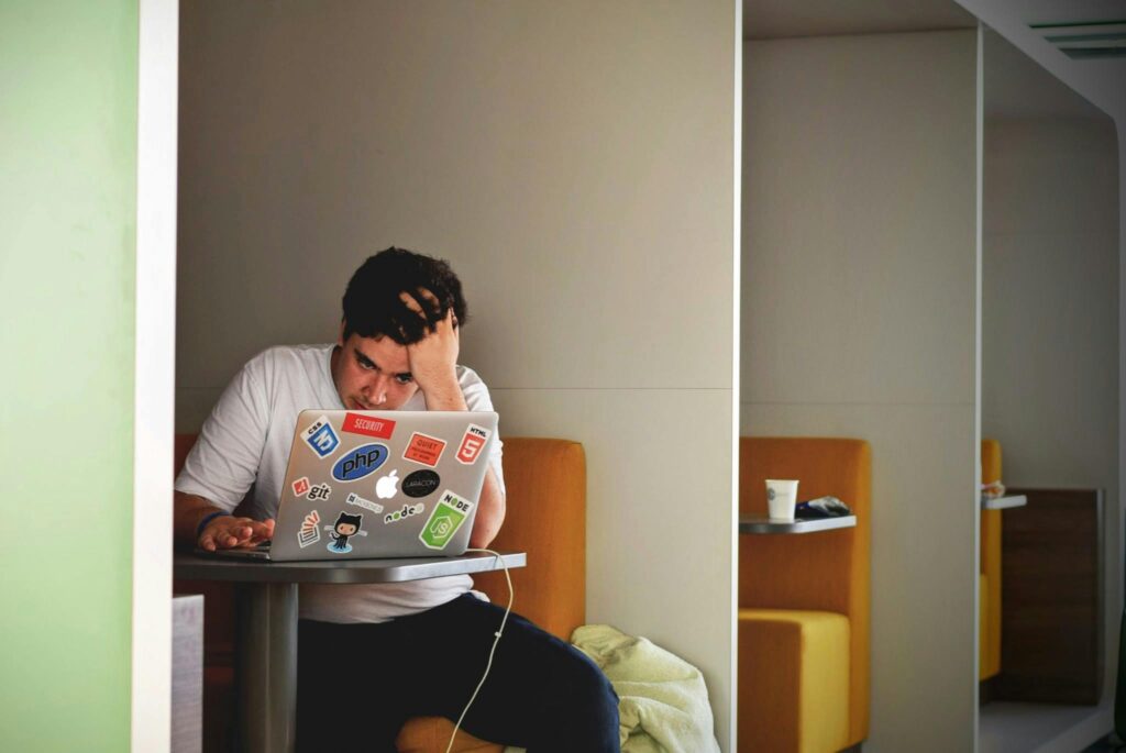 Man working on his PC, looking stressed, embodies the struggle of overcoming challenges in a demanding work environment.