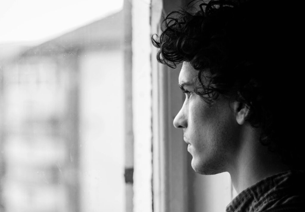 A man looks out a window with a stressed expression on his face.