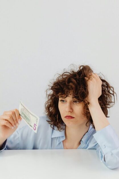 Curly-Haired Woman Holding Paper Money on White Background, Representing Inflation and Financial Stress