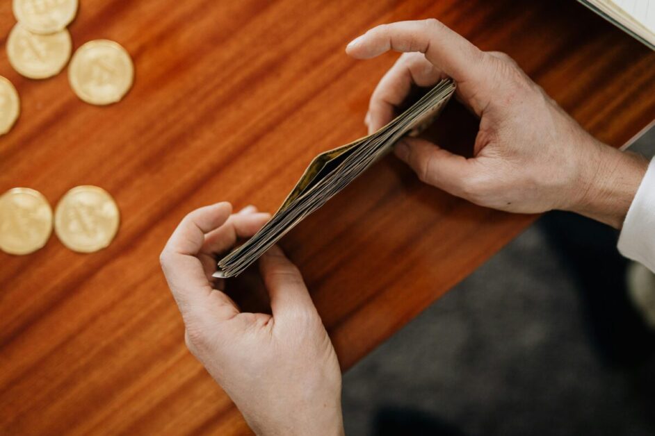 Hands carefully counting and organizing a stack of US dollar bills, representing the careful management of finances and money-saving challenges.