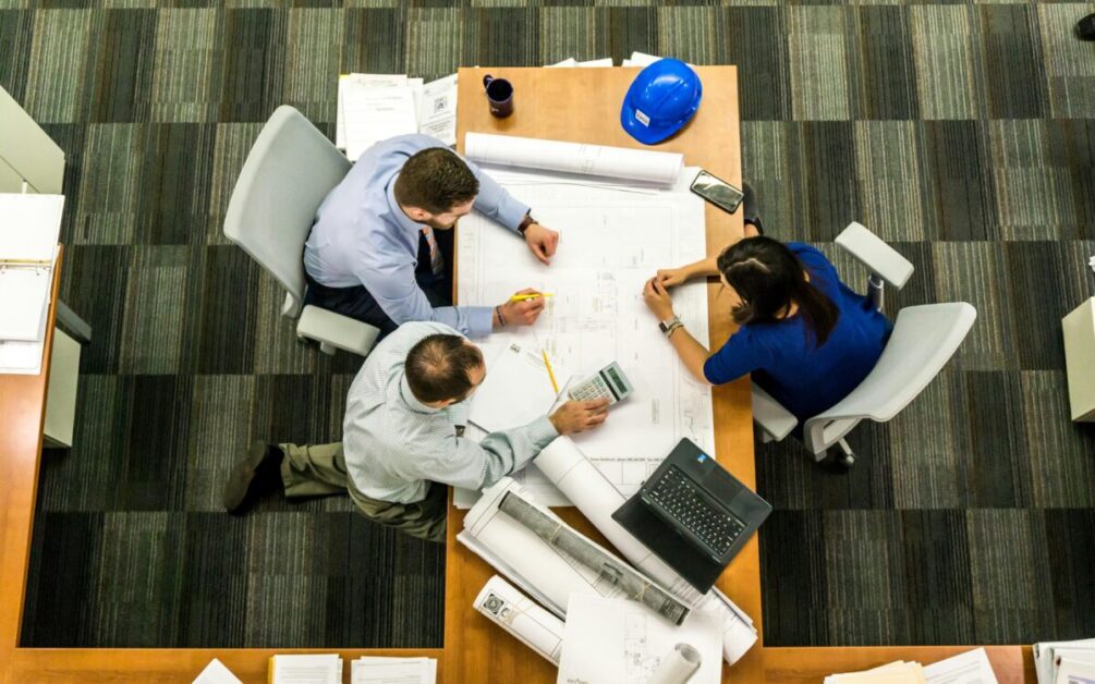 A team of professionals collaborating on a blueprint at an office table, fostering skill development through teamwork and problem-solving.