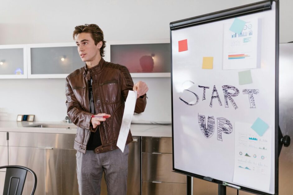 Entrepreneurial mindset shown by a young man presenting startup ideas next to a whiteboard with 