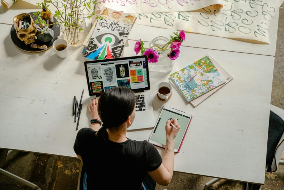 A designer working on a laptop and tablet in a creative workspace, emphasizing skill development in graphic design and creativity.